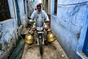 Ein Milchverkäufer fährt mit seinem Fahrrad durch eine enge Gasse im alten Bundi, Rajasthan. Diese historische Stadt ist berühmt für das beeindruckende Taragarh Fort und mehr als 50 in die Erde reichende Stufenbrunnen, die vor dem Einzug der modernen Technik zur Wasserversorgung genutzt wurden - Foto von  Oscar Espinosa