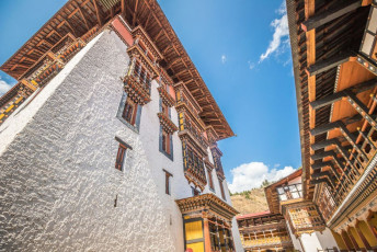Ein Foto aus dem Innenhof des Dzong von Thimphu, Bhutan, zeigt die eindrucksvollen Holzverzierungen an den Fenstern und Dächern. Im Inneren des großen Komplexes befinden sich dreißig Tempel, Schreine und Kapellen