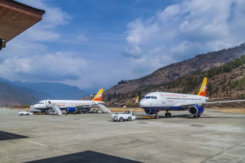 Zwei Flugzeuge des Typs Airbus A319 der Drukair Royal Bhutan Airline auf der Landebahn des internationalen Flughafens Paro, einem der schwierigsten anzufliegenden Flughäfen der Welt, da die umliegenden Gipfel bis zu 5.500 m hoch sind. Nur wenige Piloten sind für die Landung auf diesem Flughafen zugelassen © Kateryna Mashkevych