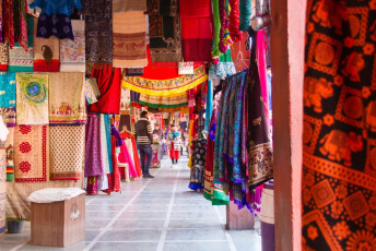 Ein farbenfroher Stoffmarkt mit Besuchern, die in der historischen Stadt Jaipur, Rajasthan, Stoffe einkaufen © Nila Newsom