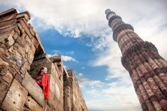 Ein Besucher betrachtet den Qutub Minar (Siegesturm) im Qutub-Moschee-Komplex in Alt Delhi. Die Oberfläche des Turms ist kunstvoll mit geometrischen Mustern und Inschriften aus dem Koran verziert © Pikoso.kz