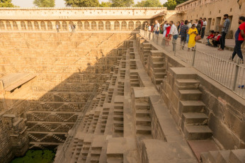 Touristen bewundern den alten Chand Baori in Abhaneri, Rajasthan. Es handelt sich um einen der tiefsten und größten Stufenbrunnen der Welt, der zur Wasserspeicherung diente. Er reicht 13 Stockwerke in die Tiefe und beherbergt auf der anderen Seite einen Tempel sowie einen Palast, der später hinzugefügt wurde © Amlan Mathur / Shutterstock