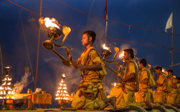 Junge Priester knien am Ufer des Ganges in Varanasi nieder, um Aarti, eine hinduistische Zeremonie, zu begehen, bei der Gottheiten mit Lichtern verehrt werden © Roop_Dey