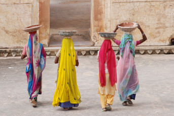 In farbenfrohe Saris gekleidete Frauen tragen im Amber Fort in Jaipur, Rajasthan, anmutig ihre Tongefäße auf dem Kopf © RuiMSantos