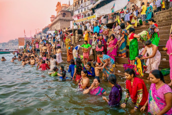Hunderte von Hindus in farbenfroher Kleidung versammeln sich an den historischen Ghats des Ganges in Varanasi, um sich durch ein Bad im Wasser des Flusses von ihren Sünden zu reinigen © CherylRamalho