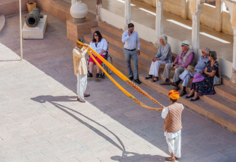 Touristen sehen zu, wie ein Reiseführer sie im Museum im Fort Mehrangarh, Rajasthan, in die Kunst des Turbanwickelns einweist. Für einen Turban wird ein 3 bis 6 m langer Stoff verwendet.