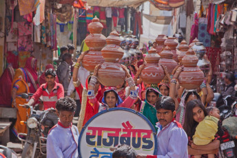 Erleben Sie die Pracht einer traditionellen hinduistischen Hochzeitszeremonie. Die Frauen tragen symbolische Schüsseln durch die Straßen von Deogarh, einer Stadt in Rajasthani, während die Band vorausgeht und fröhliche Musik spielt. © pjhpix / Shutterstock