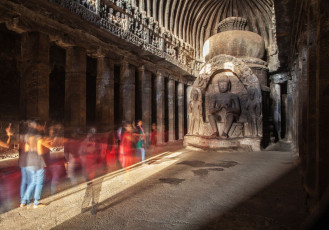 Eine Buddha-Statue erstrahlt im Sonnenlicht in einer der schmalen, rechteckigen Gebetshallen mit ihren charakteristischen hohen geschwungenen Decken im Ajanta-Höhlenkomplex bei Aurangabad.