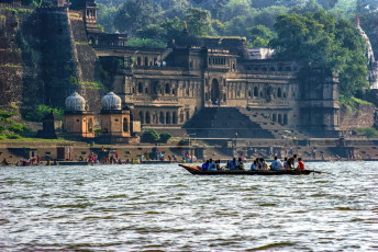 Touristen bewundern das beeindruckende Maheshwar Fort in Madhya Pradesh von einem Boot auf dem Fluss Narmada aus. Wegen der Schönheit dieses Wahrzeichens wurde schon so mancher Bollywood-Film an diesem Ort gedreht.