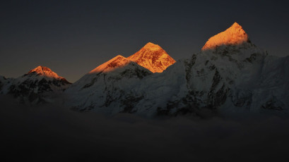 Ein spektakulärer Anblick der Gipfel des Everest, Khumbutse und Nuptse im Licht der untergehenden Sonne. Die Gipfel scheinen sich aus der Wolkenbank zu erheben, die den unteren Teil der Berge bedeckt. © perreten
