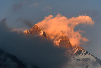 Die Gipfel des Lhotse tauchen aus den Wolken auf und fangen die Sonnenstrahlen des späten Nachmittags in Dingboche ein. Dingboche ist ein beliebter Zwischenstopp für Bergsteiger, die sich ein oder zwei Tage an die Höhe gewöhnen, bevor sie zum Everest Basislager weiterziehen. © Jaturapat Suasongsin