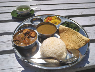 Dal bhat, ein herzhaftes traditionelles nepalesisches Gericht, das aus Linseneintopf, gedämpftem Reis, Gemüse, Hühnercurry, Poppadum und Gewürzen besteht. Es ist ein Standardgericht für Einheimische und Touristen gleichermaßen. © Andrey Rykov