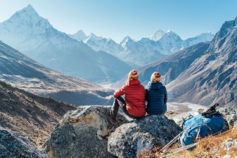 Zwei Bergsteiger legen ihre Tagesrucksäcke und Wanderstöcke für eine Weile ab und setzen sich, um die atemberaubende Aussicht auf das Tal zu bewundern. In der Ferne sind die Gipfel des 6812 m hohen Ama Dablam und des 6495 m hohen Tobuche zu sehen. Das Bild wurde außerhalb von Dughla aufgenommen, südlich des Khumbu-Gletschers. © Solovyova