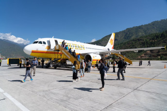 Touristen kommen in einem Flugzeug der Bhutan Airlines auf dem internationalen Flughafen von Paro an. Aufgrund der hohen Berggipfel, die den Flughafen umgeben, sind nur wenige Piloten berechtigt, hier zu landen © charnsitr