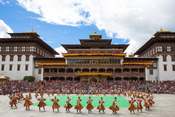 Tausende von Menschen strömen von nah und fern herbei, um das farbenfrohe Maskentanzfestival im riesigen Hof des Thimphu Dzong in Bhutan mitzuerleben. Beim Tshechu-Festival werden die guten Taten von Guru Rinpoche mit traditionellen Liedern und Tänzen von Männern und Frauen in farbenfrohen Kostümen gefeiert © Sammy L