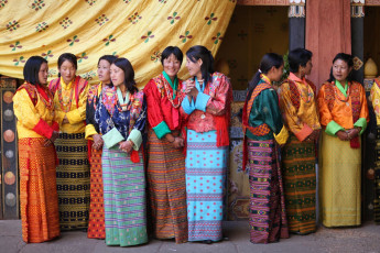Frauen in farbenfrohen traditionellen Kleidern warten auf ihren Auftritt während des Tshechu-Festivals in Paro, Bhutan. Dieses Maskentanzfest ist das wichtigste religiöse Fest im Königreich Bhutan © Feije Riemersma