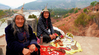 Zwei ältere einheimische Frauen verkaufen Lebensmittel an der Hängebrücke von Punakha, die über den Po Chhu-Fluss führt. Sie ist die zweitlängste Brücke in Bhutan und verbindet das alte Stadtzentrum von Punakha mit dem Rest des Tals. Diese Eisenkettenbrücke ist eine beliebte Touristenattraktion © Alp Galip