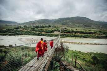 Mönche überqueren eine lange Hängebrücke über einen Fluss im Königreich Bhutan © Dylan Haskin