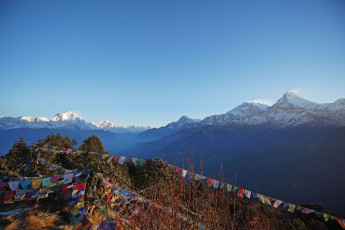 Eine typische nepalesische Berglandschaft mit schneebedeckten Gipfeln, welche die letzten Sonnenstrahlen reflektieren, mit Gebetsfahnen im Vordergrund © Chettarin