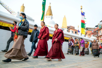 Pilger und buddhistische Mönche gehen im Uhrzeigersinn um die berühmte Boudhanath Stupa in Kathmandu. Dies ist eine meditative Praxis, die dem negativen Karma entgegenwirken soll © Bim