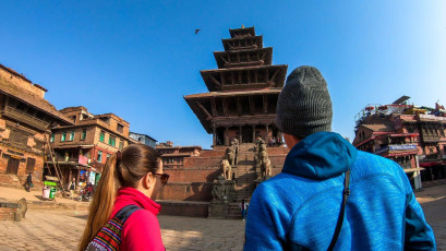 Ein Touristenpaar nähert sich dem Nyatapola-Tempel auf dem Taumadhi-Platz in Bhaktapur/Nepal. Dieser fünfstöckige Tempel ist der höchste in Nepal. Er ist aus Holz und Ziegeln erbaut und mit prächtigen Schnitzereien versehen - ein Ort der Spiritualität und der Hingabe für Menschen aus nah und fern © Christopher Moswitzer