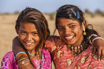 Zwei lächelnde Mädchen in traditionellen Kleidern und Ornamenten in der Wüste Thar in Jaisalmer, Rajasthan, Indien © Bartosz Hadyniak