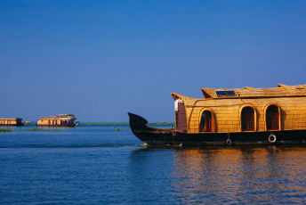 Ein Hausboot treibt friedlich auf den Backwaters von Kerala. Diese Form des Reisens ist hier bei Touristen sehr beliebt und bietet die perfekte Möglichkeit, das Alltagsleben am Ufer, die Reisfelder und die Vogelwelt in aller Ruhe zu beobachten.