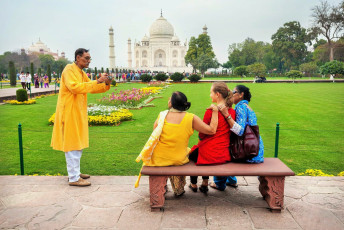 Eine indische Familie macht auf einer Bank im Garten vor dem Taj Mahal ein Bild mit ausländischen Touristen, Agra - Foto von Pikoso.kz
