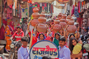 Eine Band führt Frauen mit symbolischen Krügen auf dem Kopf als Teil einer traditionellen Hindu-Hochzeitsfeier bei einer Prozession durch die Straßen der Stadt in Rajasthan – Foto von pjhpix