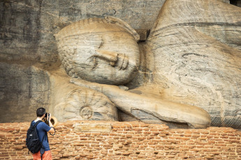Ein Besucher fotografiert den gigantischen Liegenden Buddha, der eine von vier in den Felsen gehauenen Statuen im Gal Vihara-Tempel in der antiken Stadt Polonnaruwa, nahe Kandyins darstellt, Sri Lanka © travelwild
