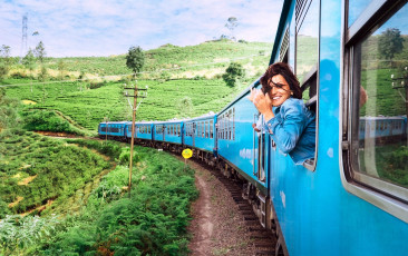 Ein Tourist in einem Zug lächelt in die Kamera. Die malerische Bahnstrecke zwischen Kandy und Nuwara Eliya, Sri Lanka, führt die Reisenden an Teeplantagen, einem Wasserfall und dichten Wäldern vorbei © solovyova