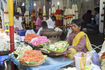Eine lange Gasse mit indischen Blumenhändlern, die auf dem Devaraja-Markt in der Stadt Mysore, Karnataka, Indien, frische Blumen und Girlanden an die Kunden verkaufen © fotoember
