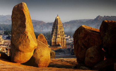 Ein majestätischer Anblick des historischen Tempelkomplexes von Hampi, der, umgeben von Felsen im Bundesstaat Karnataka, unter der hellen Sonne erstrahlt.  © Djuly