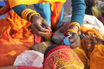 Eine weibliche Sadhu malt den Bindi als Teil der Segnung auf das Gesicht einer Frau, nachdem sie ein Bad im Ganges genommen hat - Foto von Wkok