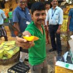ein obstverkäufer im crawford market area bietet ein stück alphonso-mango an