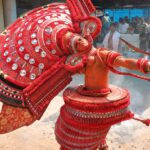 Eine Tänzerin mit roter Kopfbedeckung bei einer traditionellen Theyyam-Zeremonie Kannur