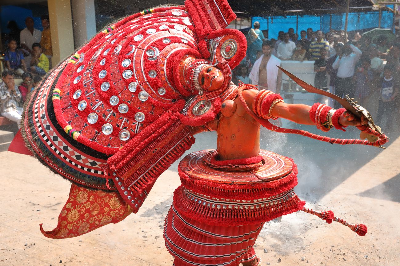 Eine Tänzerin mit roter Kopfbedeckung bei einer traditionellen Theyyam-Zeremonie Kannur